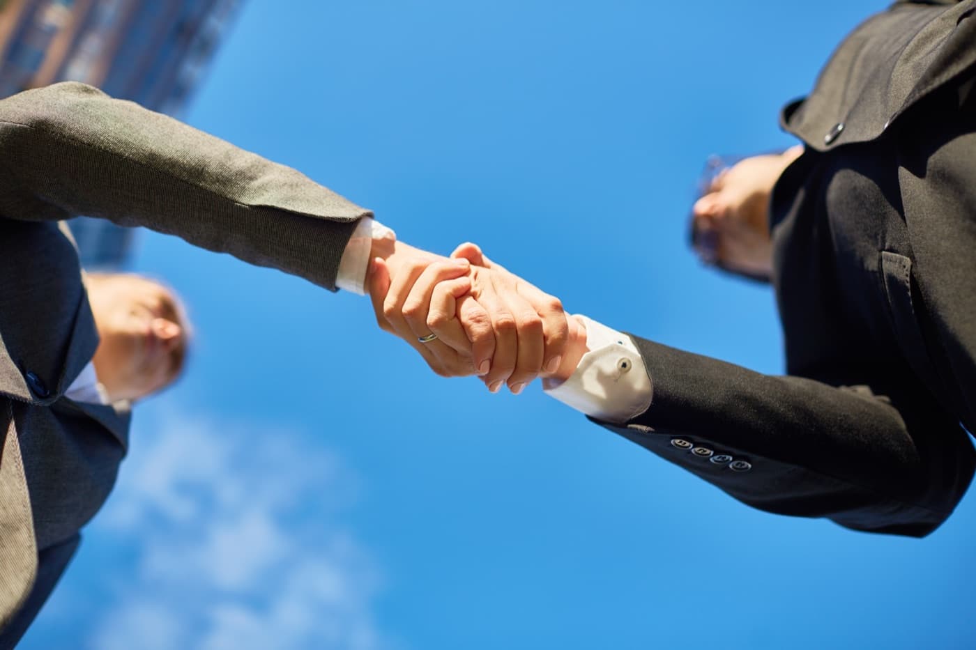 Two business people shaking hands against a clear sky